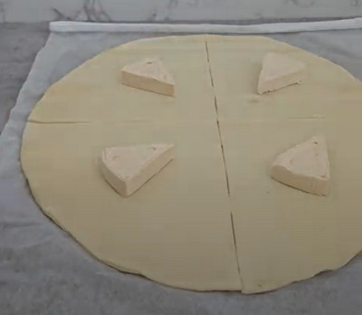 Boule de pâte à pizza garnie de Vache qui rit, aplatie au rouleau