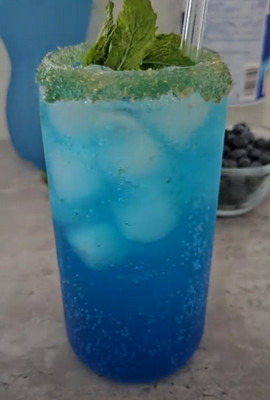 Cocktail Océan servi avec une paille, des myrtilles et de la menthe